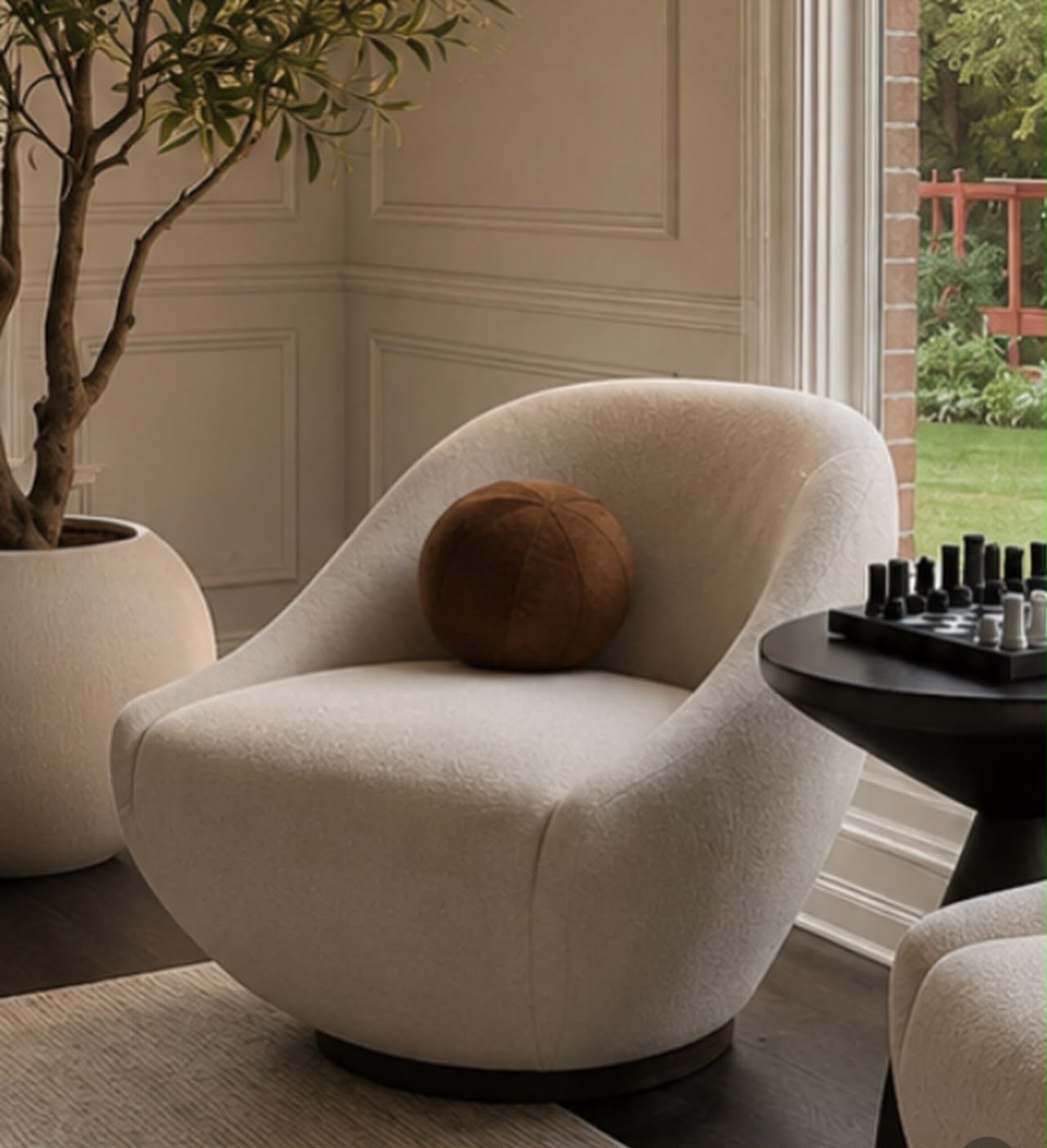 Cream bouclé swivel chair beside an olive tree and a black chess table