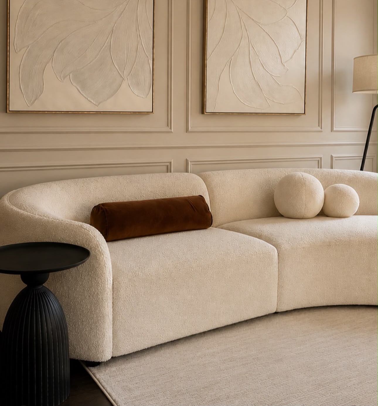 Curved cream bouclé sofa beneath textured leaf artwork
