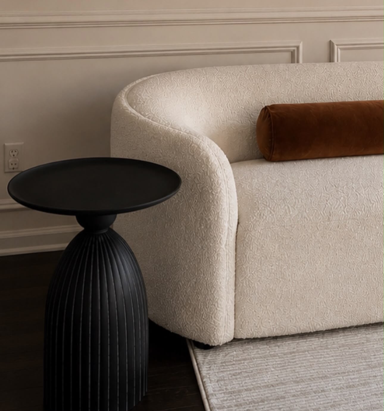 Detail of bouclé sofa arm beside a black fluted side table